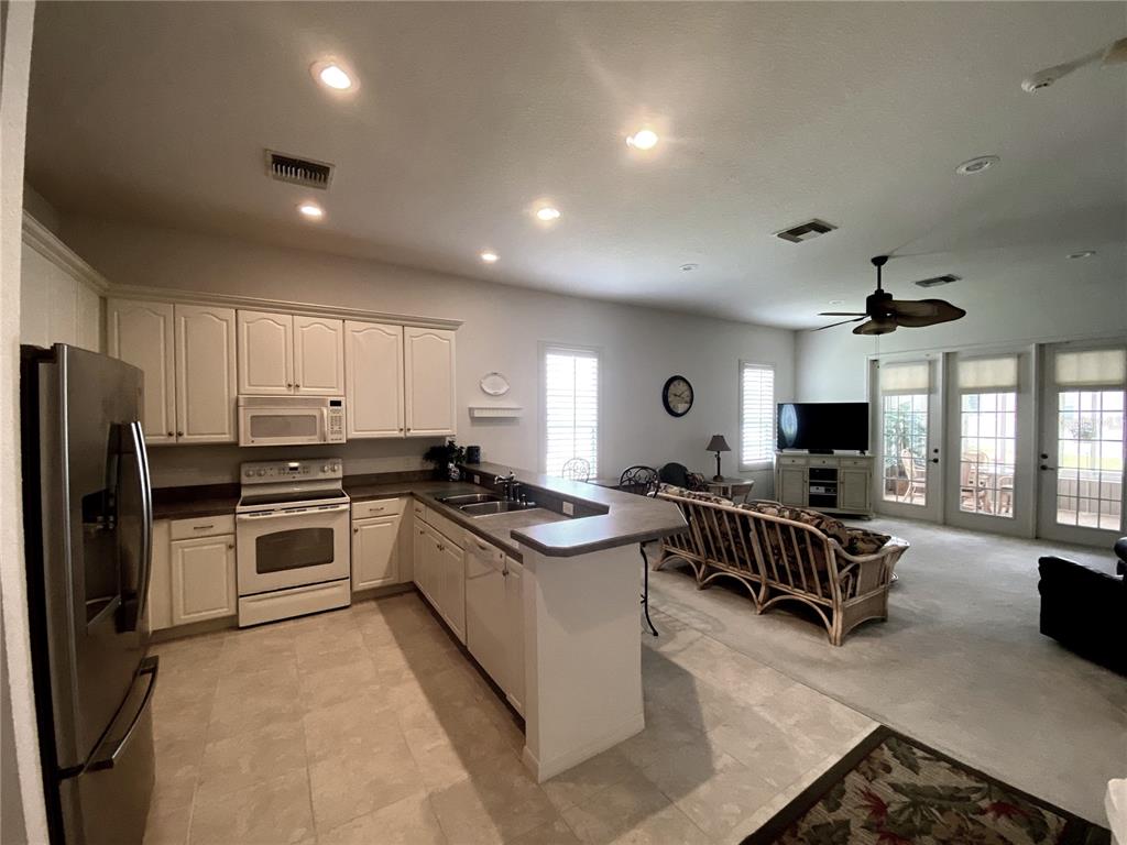 A kitchen features white cabinetry, stainless steel appliances, and a gray countertop breakfast bar — 323 TRAVELERS DRIVE, POLK CITY, FL