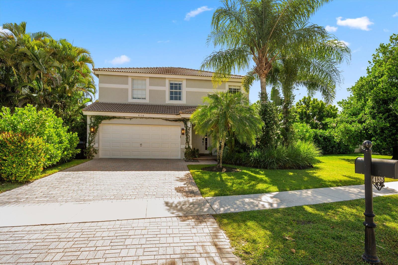 A two-story house with a paved driveway, a garage, and lush landscaping under a blue sky — 4138 Bluff Harbor Way, Wellington FL 33449, WELLINGTON, FL