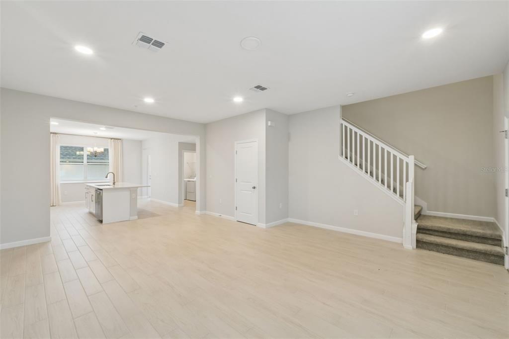 An open-concept living area features light wood-look tile flooring, a kitchen island, and carpeted stairs — 827 CREEPING FIG STREET, APOPKA, FL