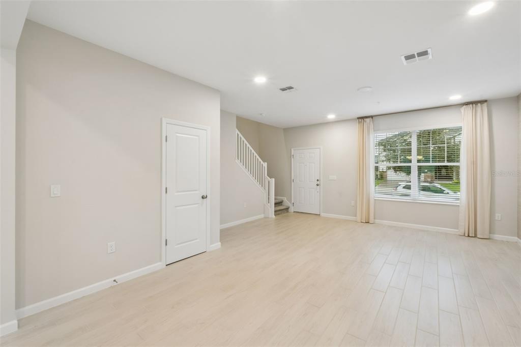 An empty living room features light-colored tile flooring, a white staircase, and a front door — 827 CREEPING FIG STREET, APOPKA, FL