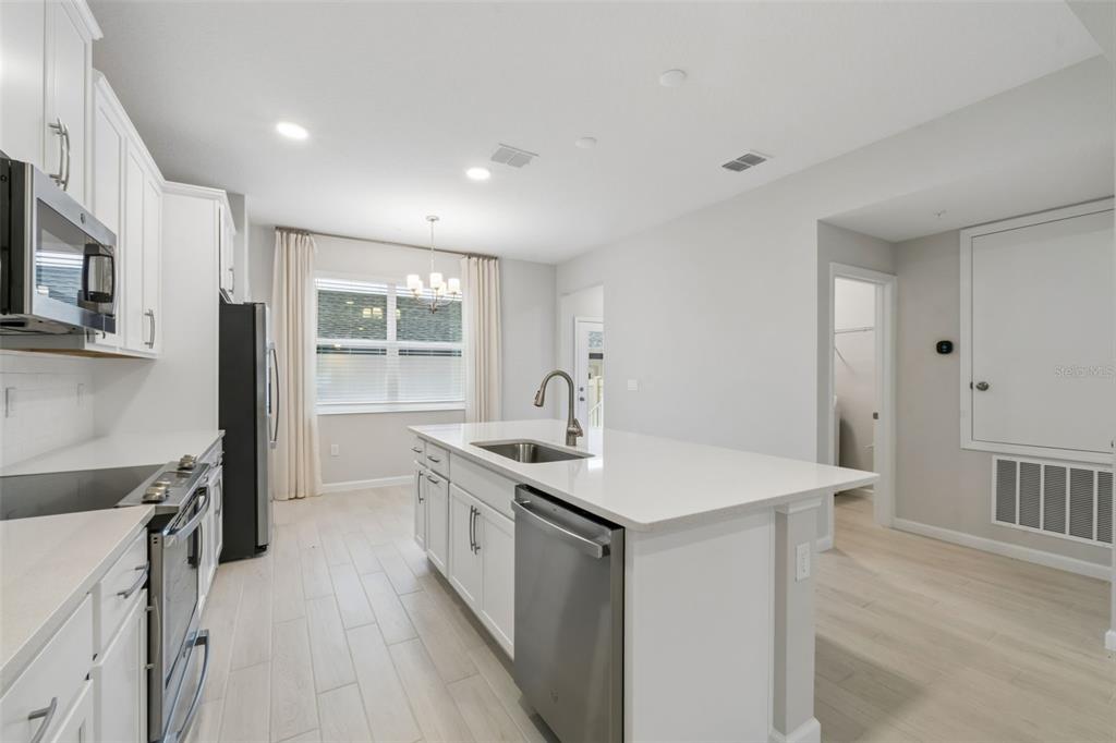 A modern kitchen features white cabinetry, a central island with a sink, and light flooring — 827 CREEPING FIG STREET, APOPKA, FL