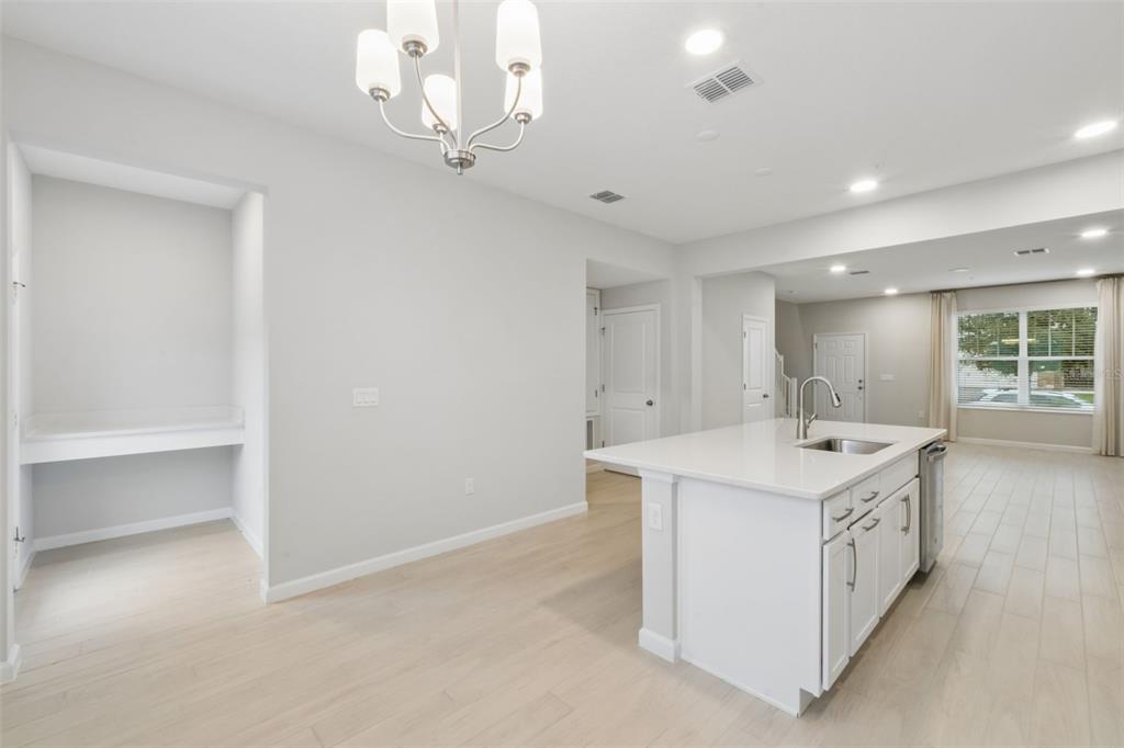 A kitchen with a white island, light wood-look flooring, and a built-in desk area — 827 CREEPING FIG STREET, APOPKA, FL