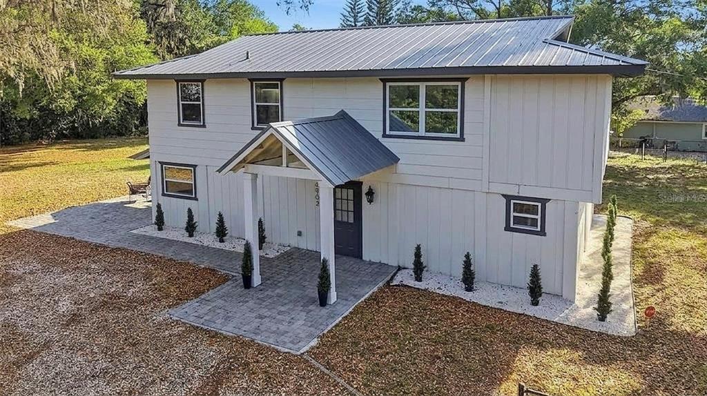 A two-story house with white vertical siding, a metal roof, and a paved entryway — 6902 E 29TH AVENUE, TAMPA, FL