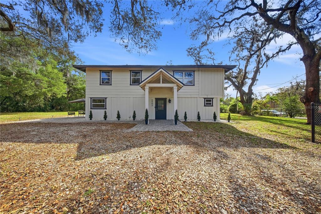 A two-story house with light siding, a dark front door, and a gravel driveway — 6902 E 29TH AVENUE, TAMPA, FL