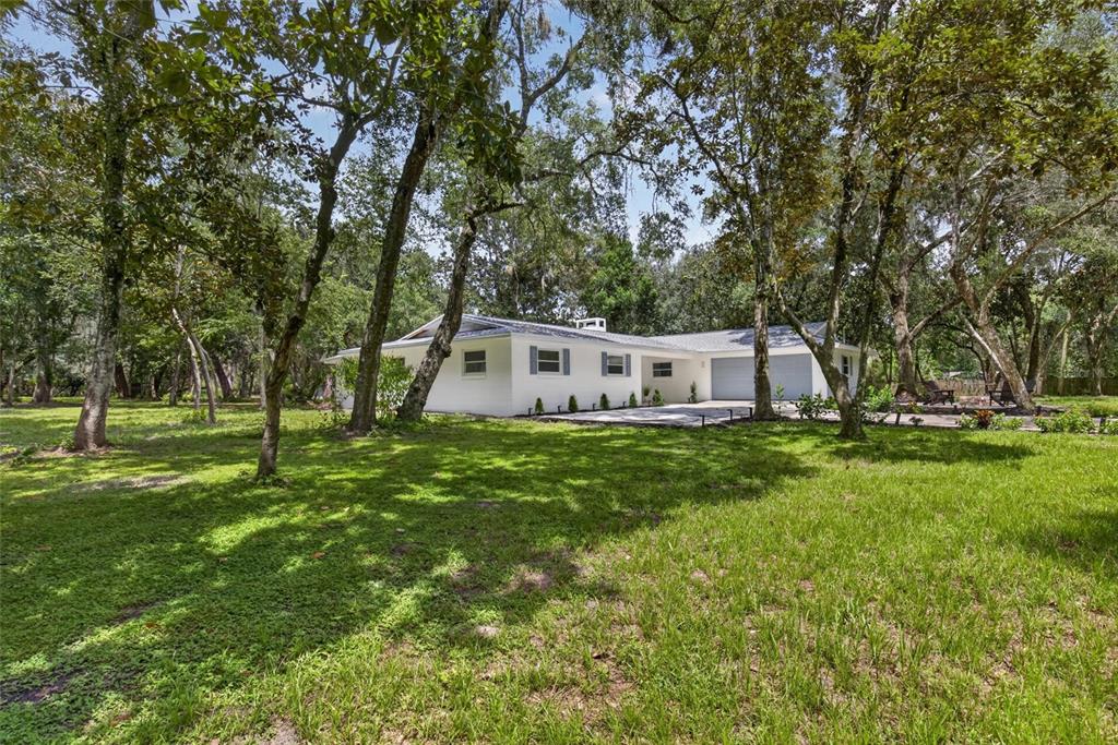 A white single-story house with a garage sits on a grassy lot among many trees — 300 SCOTT ROAD, GENEVA, FL