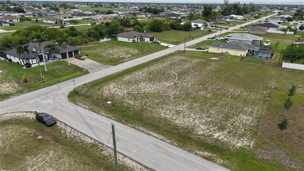 An aerial view shows a vacant residential lot situated between two houses on a street — 2009 NW 2ND AVENUE, CAPE CORAL, FL