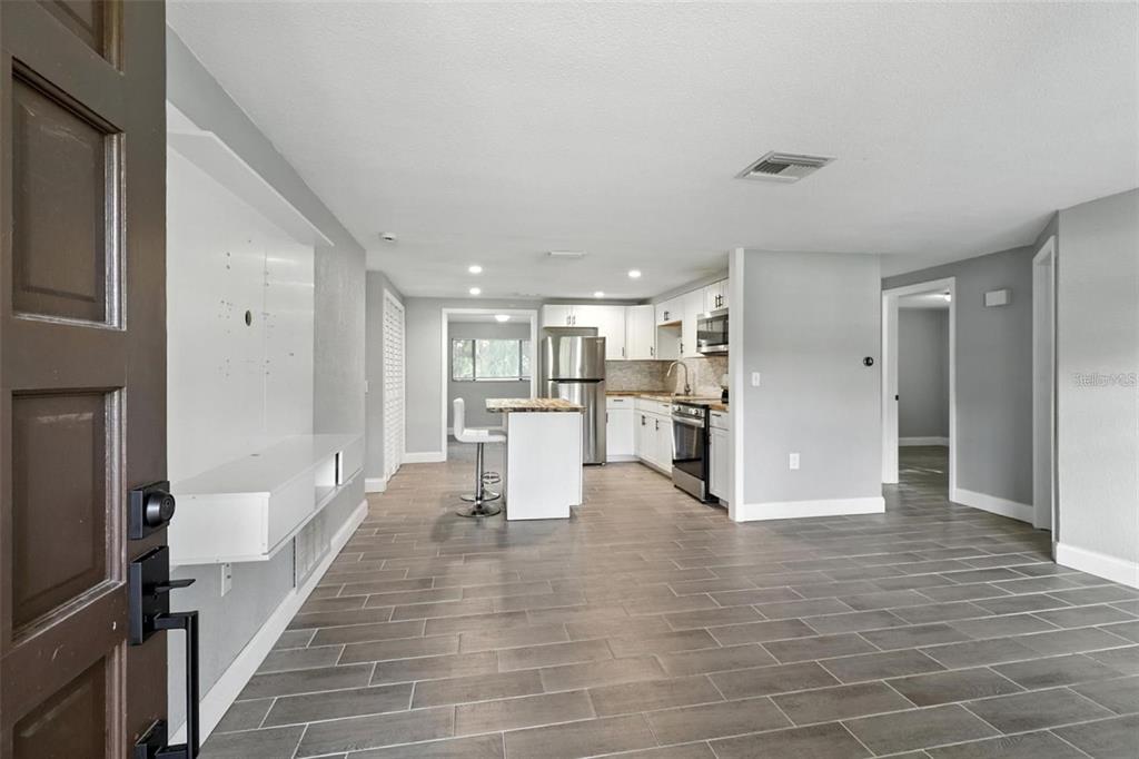 An open-concept kitchen and living area feature gray tile flooring, white cabinetry, and stainless appliances — 8035 GULF WAY, HUDSON, FL