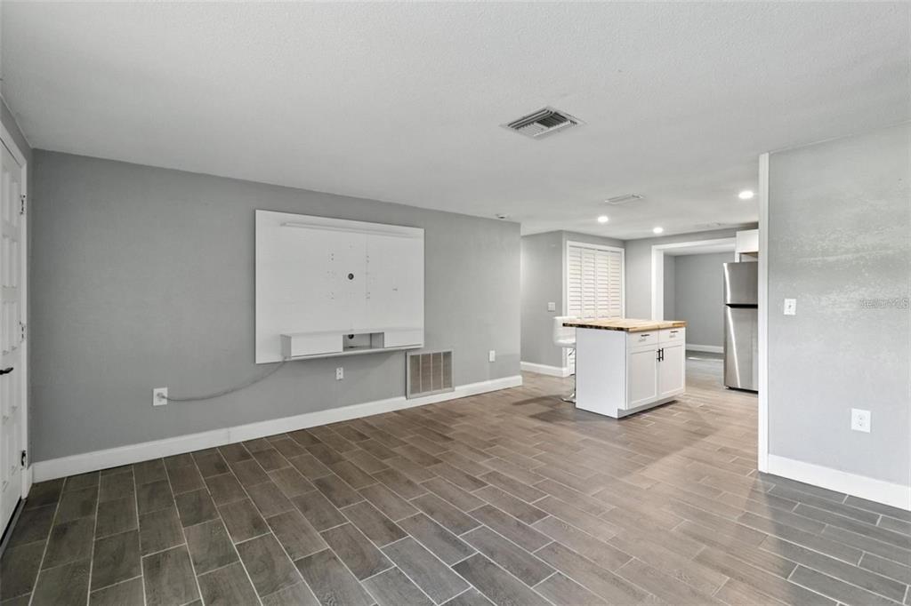 An open-concept living area features gray tile flooring, a white media console, and a kitchen — 8035 GULF WAY, HUDSON, FL