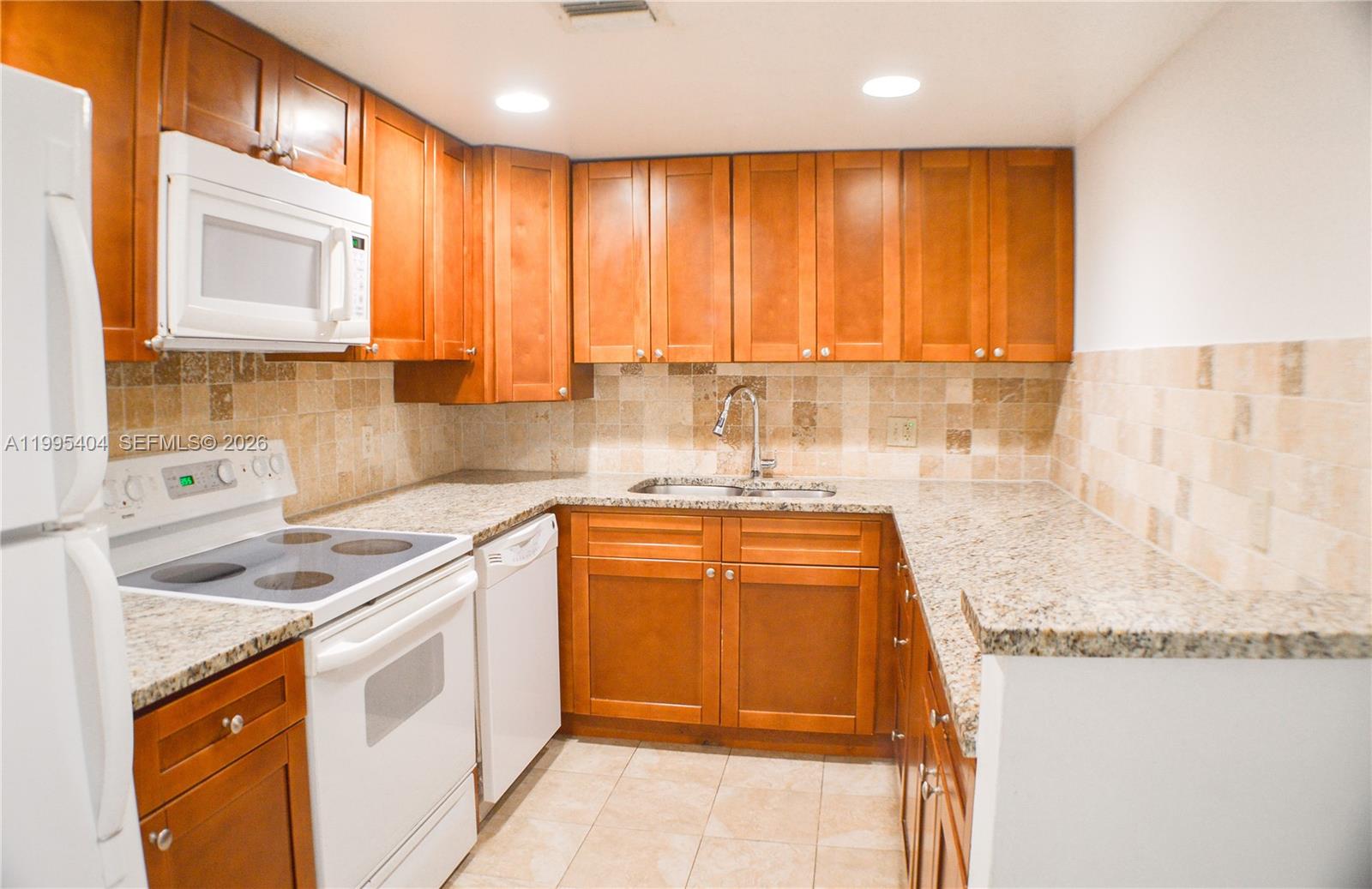 A kitchen features wooden cabinets, granite countertops, a white stove, and a tiled backsplash — 733 SE 1st Way # 206, Deerfield Beach FL 33441, DEERFIELD BEACH, FL