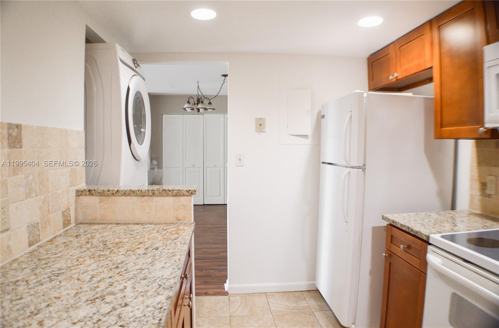 A kitchen features granite countertops, wood cabinets, a white refrigerator, and an adjacent laundry area — 733 SE 1st Way # 206, Deerfield Beach FL 33441, DEERFIELD BEACH, FL