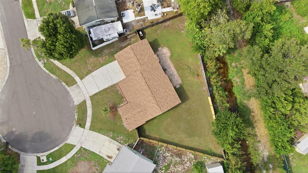 An aerial view shows a house with a brown roof, concrete driveway, and fenced backyard — 7003 LARIMER COURT, TAMPA, FL