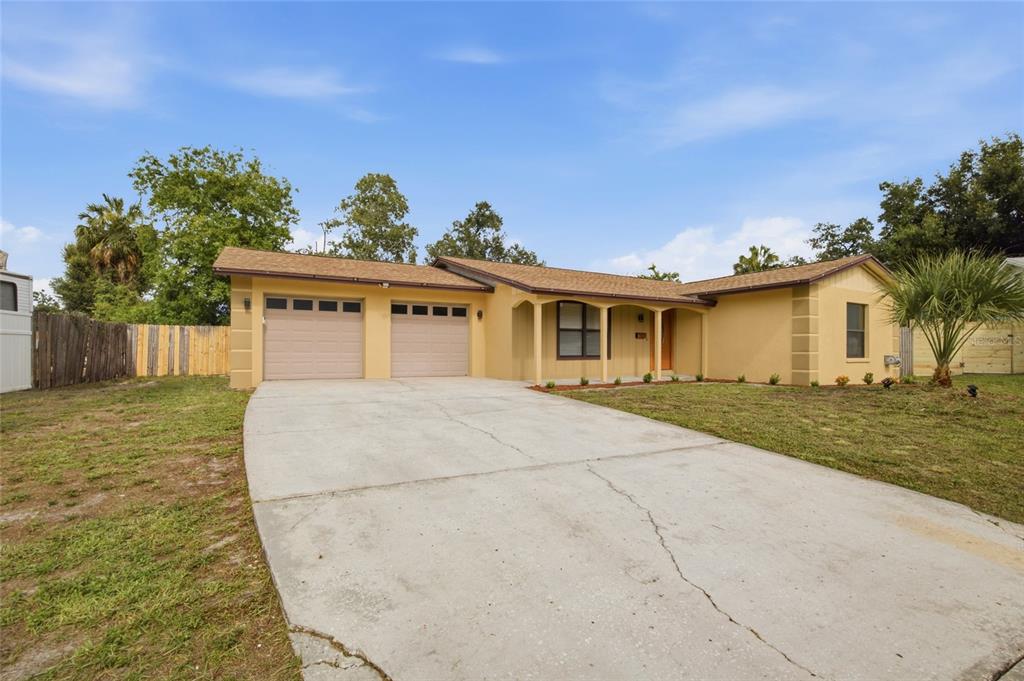 A single-story house with a two-car garage, tan stucco exterior, and a concrete driveway — 7003 LARIMER COURT, TAMPA, FL