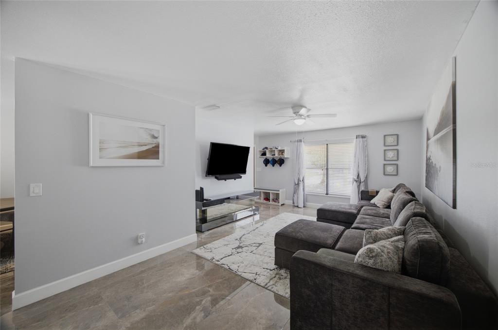 A living room with gray tile floors, a large sectional sofa, and a wall-mounted television — 7003 LARIMER COURT, TAMPA, FL