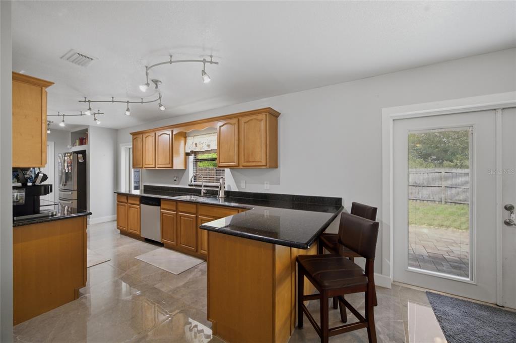 A kitchen features wood cabinets, black countertops, tile flooring, and a breakfast bar with stools — 7003 LARIMER COURT, TAMPA, FL