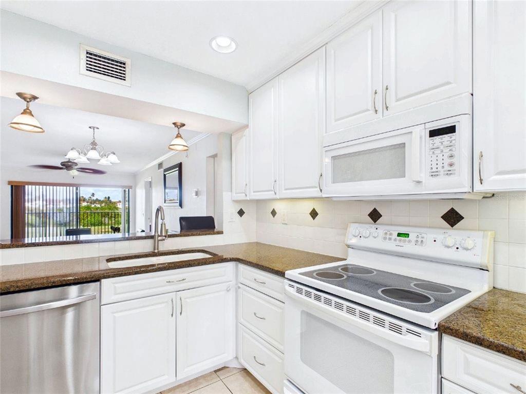 A kitchen with white cabinets, granite countertops, stainless steel appliances, and a pass-through window — 6335 PALMA DEL MAR BOULEVARD S UNIT 223, ST PETERSBURG, FL