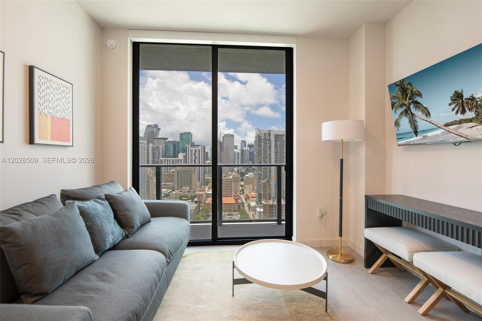 A modern living room features a gray sofa, white coffee table, and city skyline view — 121 NE 5th St # 3102, Miami FL 33132, MIAMI, FL