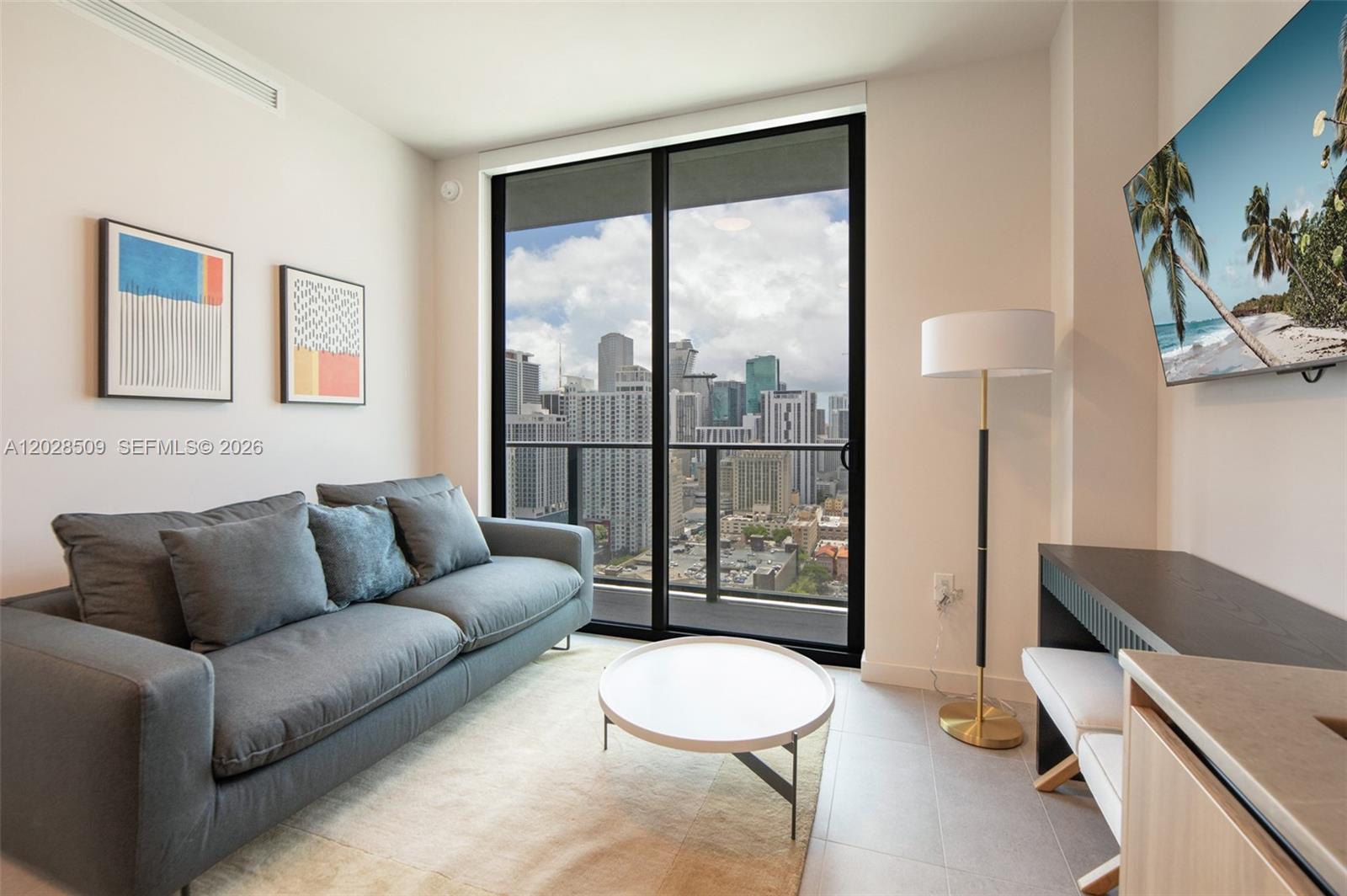 A modern living room features a gray sofa, round coffee table, and a city view — 121 NE 5th St # 3102, Miami FL 33132, MIAMI, FL