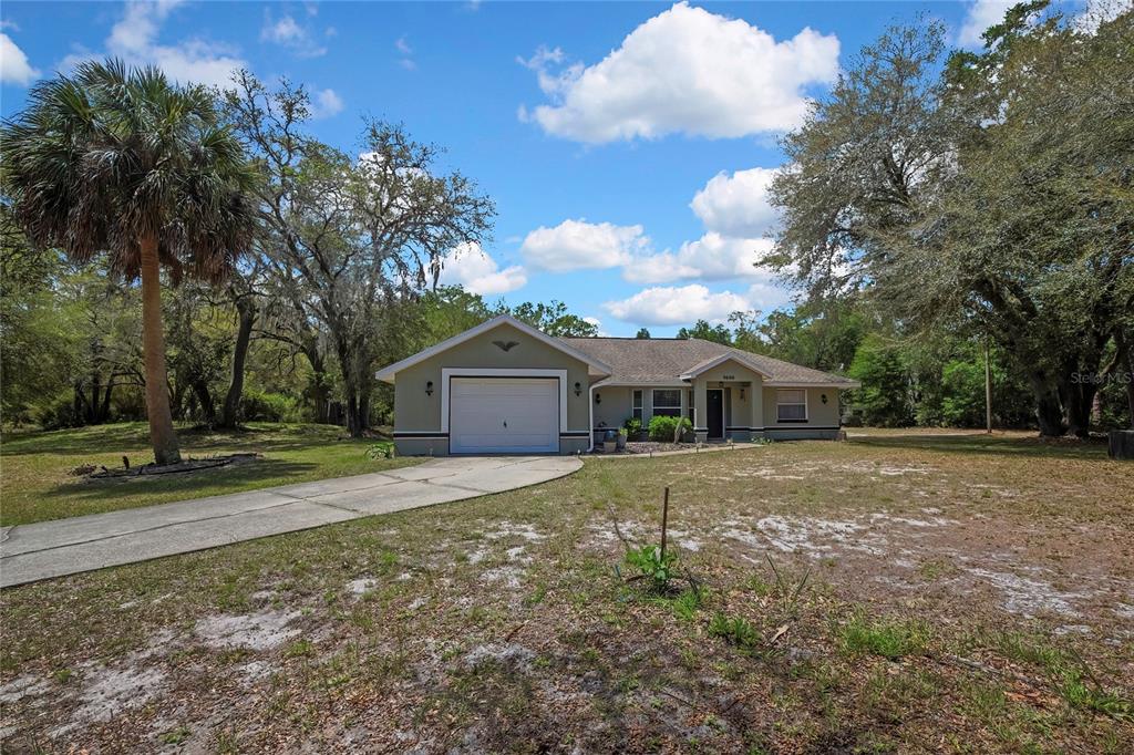 A single-story house with a garage and a concrete driveway sits on a wooded lot — 9690 N ALDER AVENUE, CRYSTAL RIVER, FL
