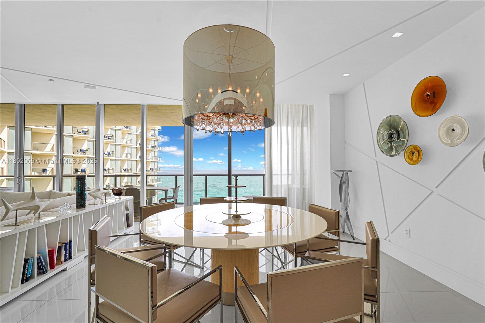 A dining room features a round table, a large drum chandelier, and ocean views — 9701 Collins Ave # 2103S, Bal Harbour FL 33154, BAL HARBOUR, FL