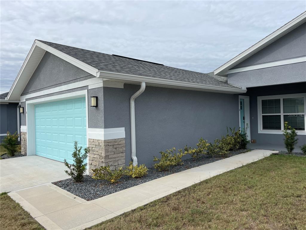 A gray house exterior with a light blue garage door, stone accents, and a concrete walkway — 110 LYNBROOK DRIVE UNIT A, PALM COAST, FL