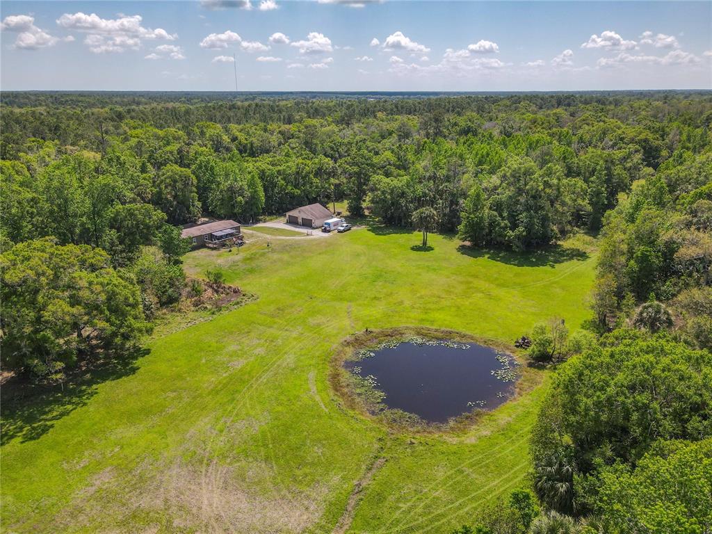 An aerial view shows a house and detached garage on a large, grassy, wooded lot — 1501 ASHBY CREEK ROAD, OSTEEN, FL