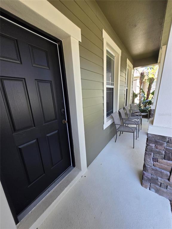 A covered front porch features a black door, olive green siding, and three metal chairs — 8451 KARPEAL DRIVE, SARASOTA, FL