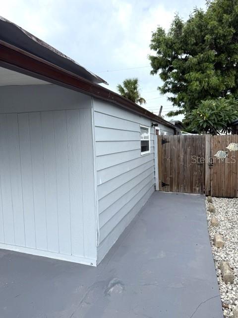 A gray-painted exterior wall with a window sits beside a wooden fence and patio — 5200 76TH STREET N, ST PETERSBURG, FL