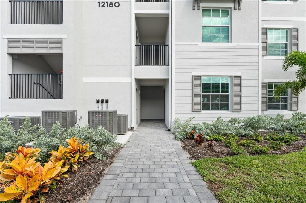 A paved walkway leads to the entrance of a multi-story apartment building with air conditioners — 12180 WELLEN GOLF STREET UNIT 108, VENICE, FL