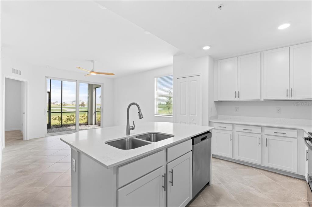 A kitchen with white cabinets, a central island with a sink, and a sliding glass door — 12180 WELLEN GOLF STREET UNIT 108, VENICE, FL