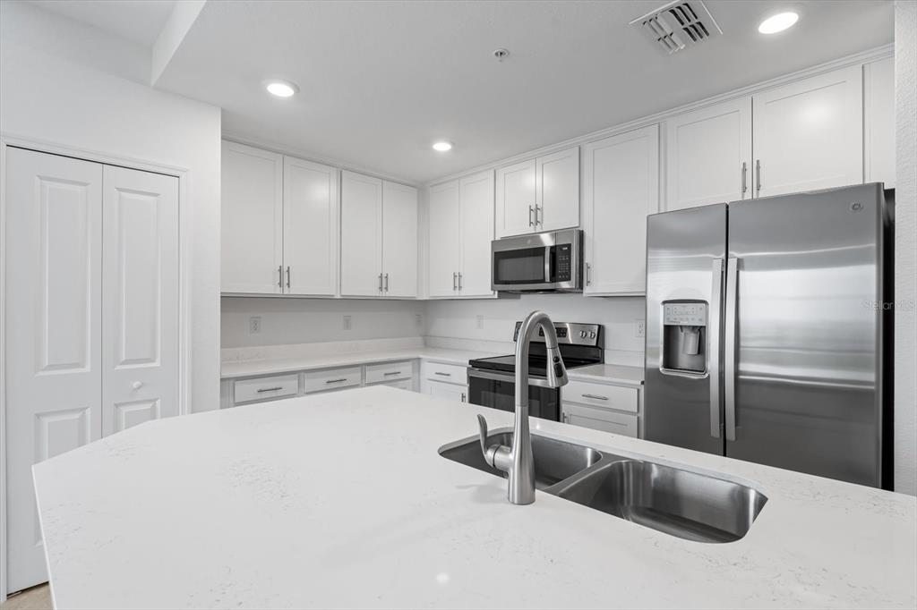 A modern kitchen features white cabinetry, stainless steel appliances, and a large quartz-topped island — 12180 WELLEN GOLF STREET UNIT 108, VENICE, FL