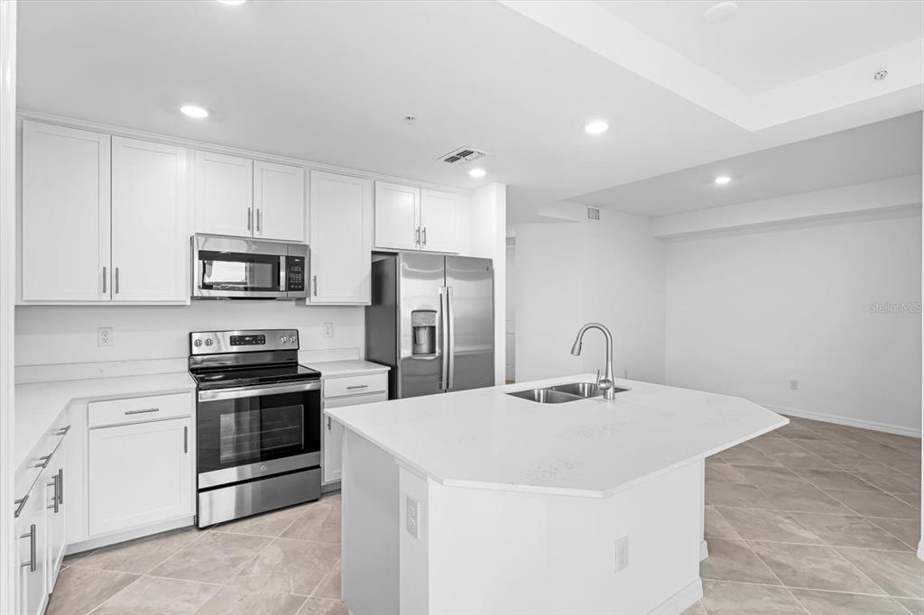 A modern kitchen features white cabinets, stainless steel appliances, and a central island — 12180 WELLEN GOLF STREET UNIT 108, VENICE, FL