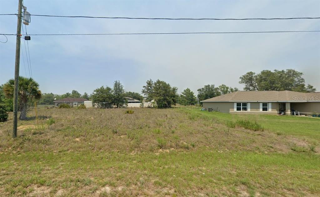 A vacant, grassy lot sits between two suburban houses under a hazy sky — MALAUKA RADIAL, OCKLAWAHA, FL