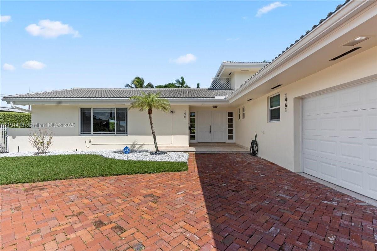 A single-story house features a brick driveway, a white garage, and a palm tree — 1961 NE 188th St, Miami FL 33179, MIAMI, FL