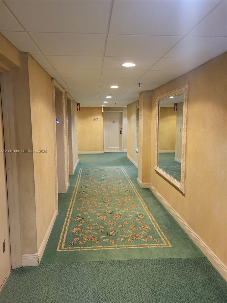 A hallway features green patterned carpet, beige walls, recessed lighting, and a large wall mirror — 2625 Collins Ave # 1601, Miami Beach FL 33140, MIAMI BEACH, FL