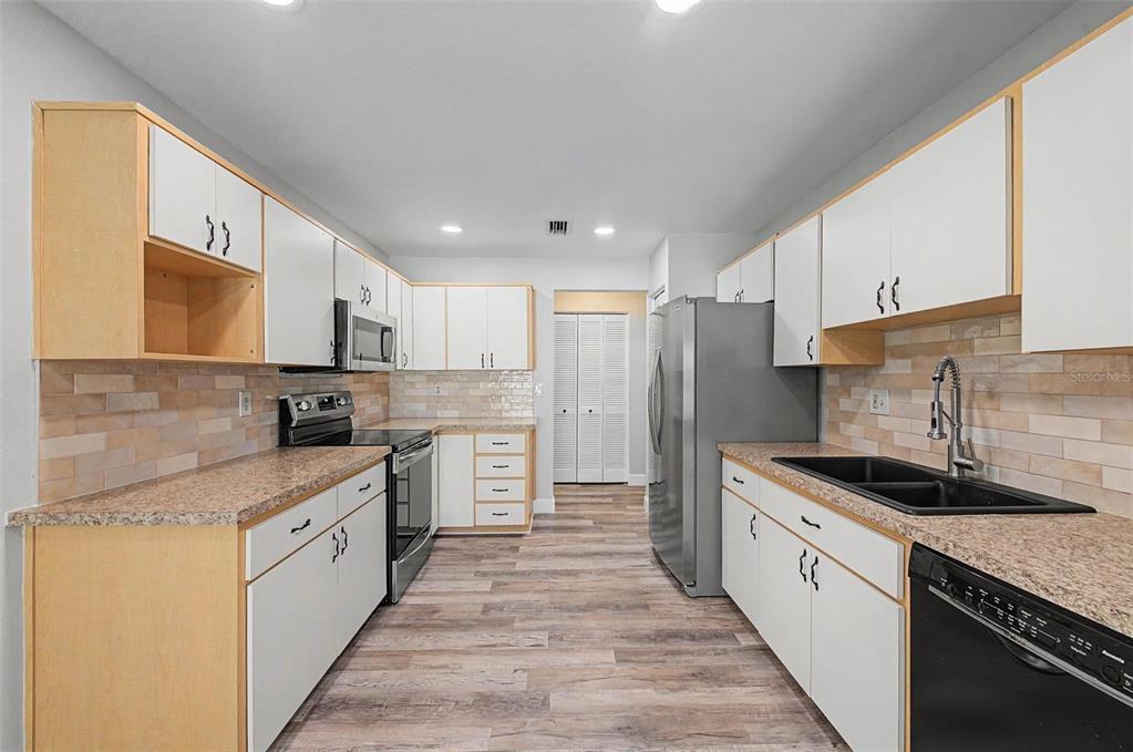 A kitchen features white cabinets, granite countertops, stainless steel appliances, and wood-look flooring — 3419 ANNETTE COURT, CLEARWATER, FL
