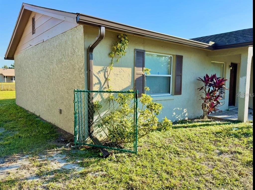 The exterior of a beige house features a brown downspout, a window with shutters, and landscaping — 133 ALDERWOOD DRIVE, KISSIMMEE, FL