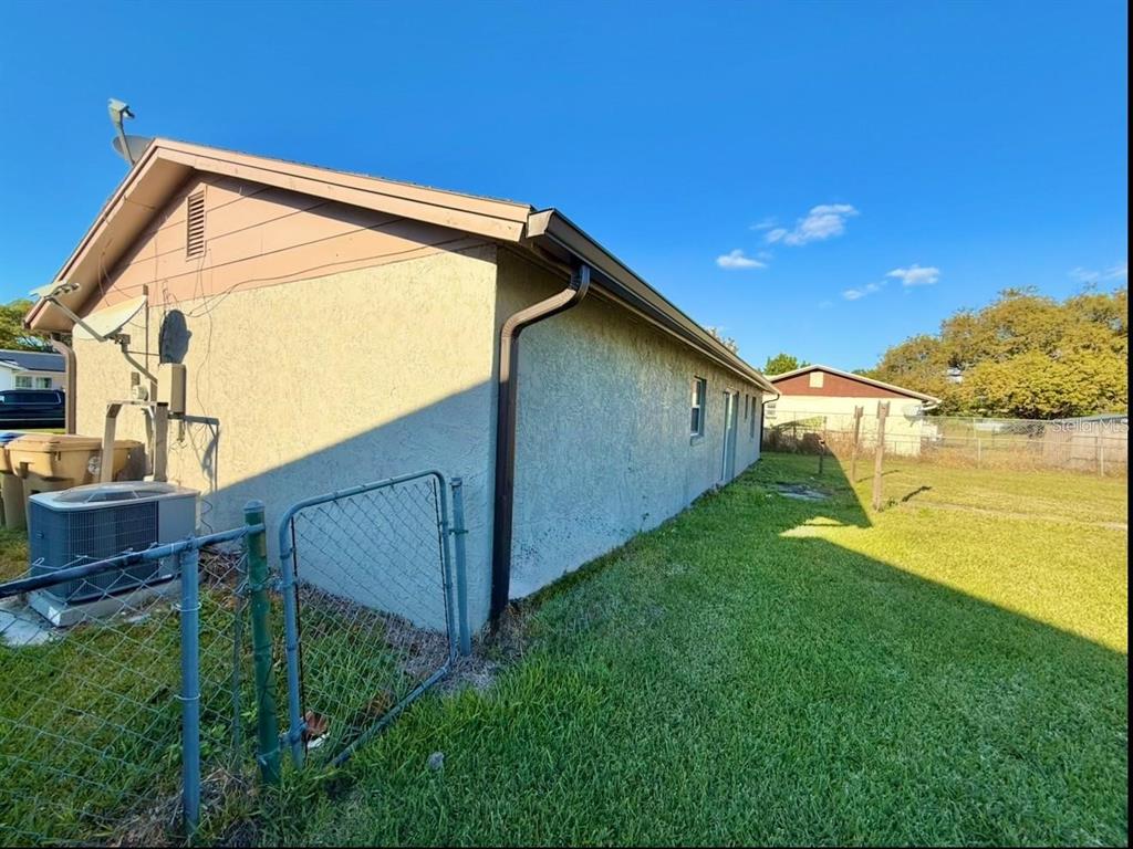 A side view of a stucco house with a metal gutter and a chain-link fence — 133 ALDERWOOD DRIVE, KISSIMMEE, FL