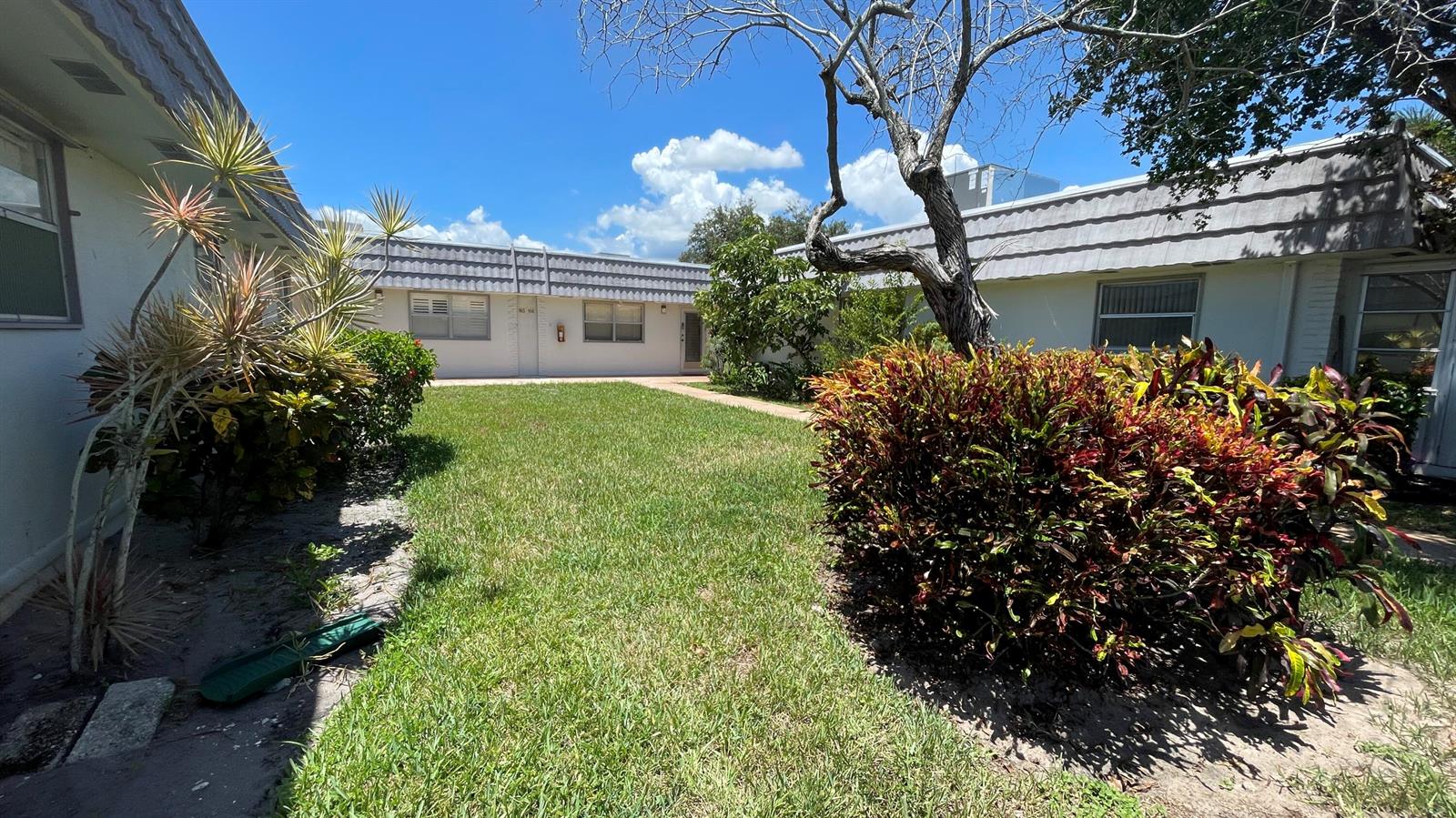 A grassy courtyard sits between two single-story apartment buildings with white walls and gray roofs — 166 Valencia G, Delray Beach FL 33446, DELRAY BEACH, FL