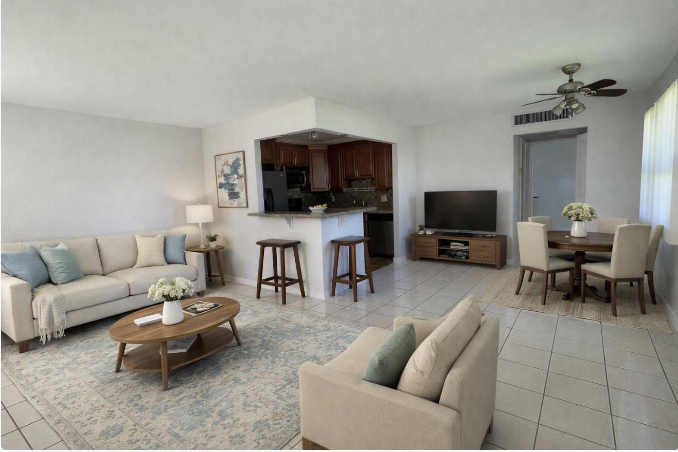 An open-concept living and dining area features tile flooring, a kitchen island, and neutral furniture — 166 Valencia G, Delray Beach FL 33446, DELRAY BEACH, FL