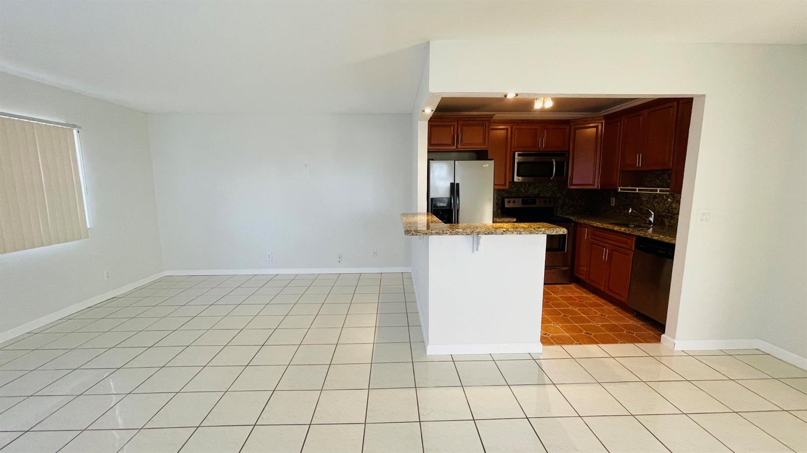 An open-concept living area with white tile floors leads to a kitchen with wood cabinets — 166 Valencia G, Delray Beach FL 33446, DELRAY BEACH, FL