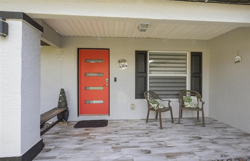 A covered front porch features a bright orange door, wood-look tile flooring, and two chairs — 10924 SW 48TH TERRACE, OCALA, FL