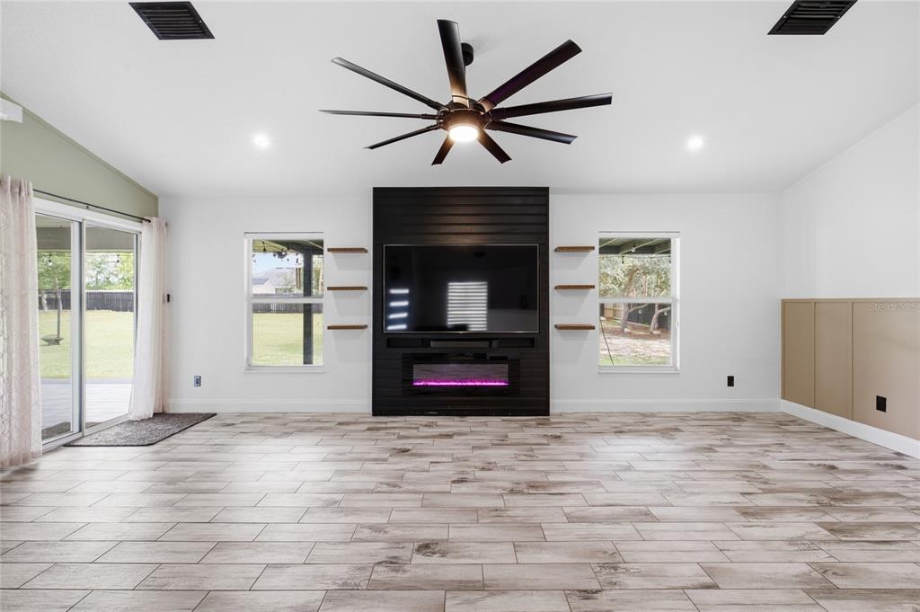 A living room features a black shiplap fireplace wall, wood-look tile flooring, and a ceiling fan — 10924 SW 48TH TERRACE, OCALA, FL