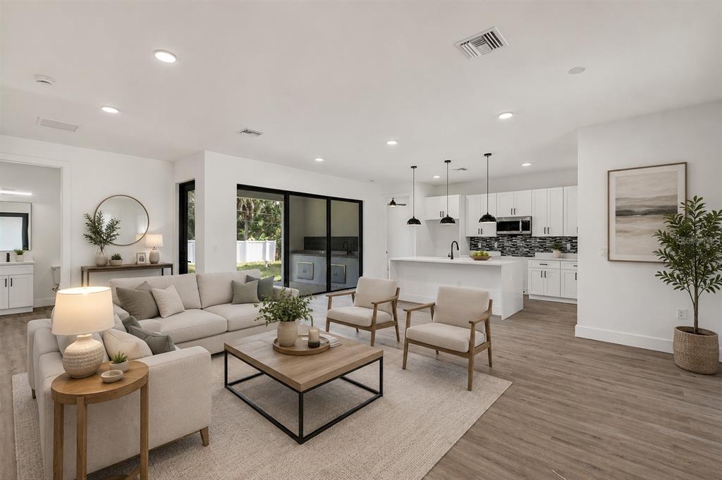 A bright, open-concept living room and kitchen featuring white cabinetry, light wood floors, and furniture — 72 SHORELAND STREET, PORT CHARLOTTE, FL