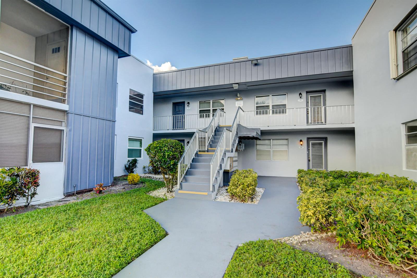 An exterior view of a two-story apartment building with a central staircase and landscaping — 42 Burgundy A # A, Delray Beach FL 33484, DELRAY BEACH, FL