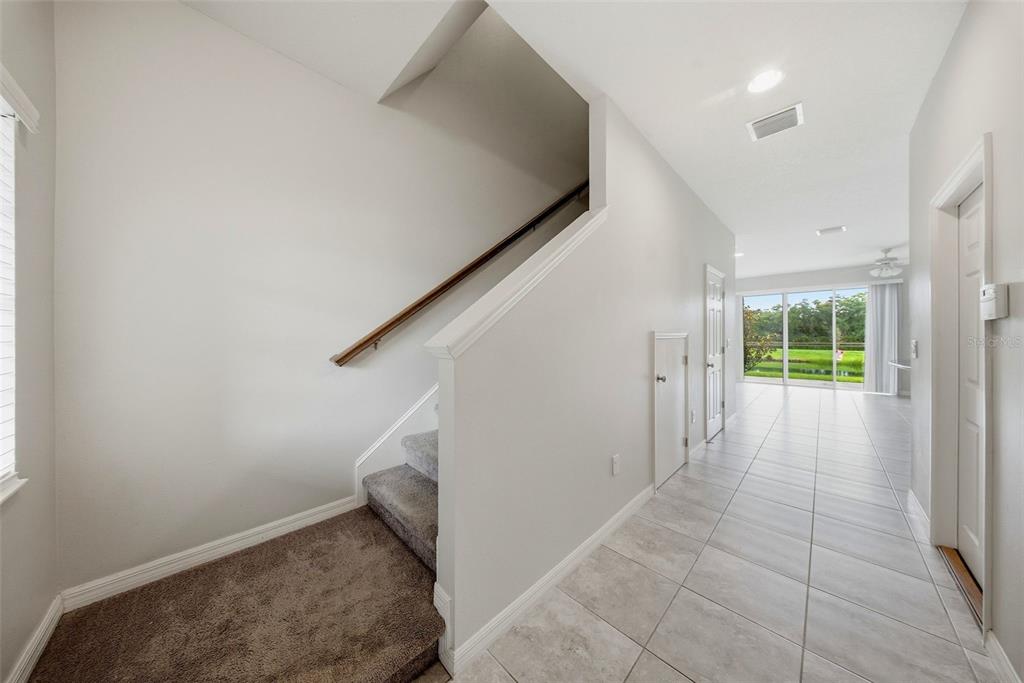 A carpeted staircase leads upstairs next to a tiled hallway with a view of outdoors — 7910 EVERGREEN CREEK COURT, RIVERVIEW, FL