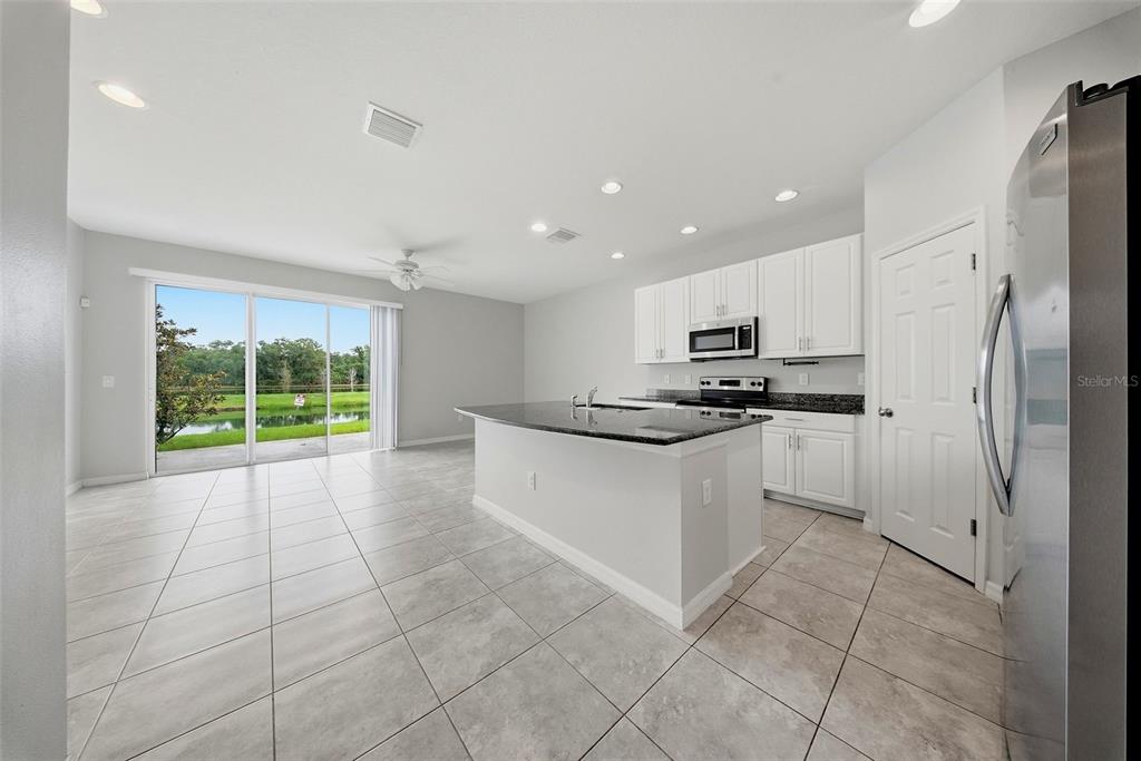 A kitchen with white cabinets, granite countertops, and tile flooring overlooks a pond through sliders — 7910 EVERGREEN CREEK COURT, RIVERVIEW, FL