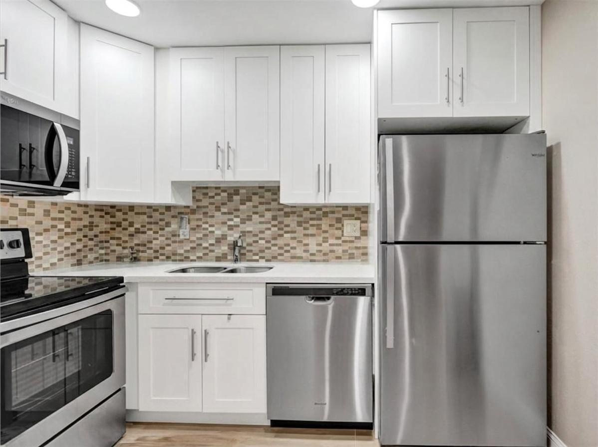 A kitchen features white cabinets, stainless steel appliances, a tiled backsplash, and light countertops — 4980 E Sabal Palm Boulevard E # 124, Tamarac FL 33319, TAMARAC, FL
