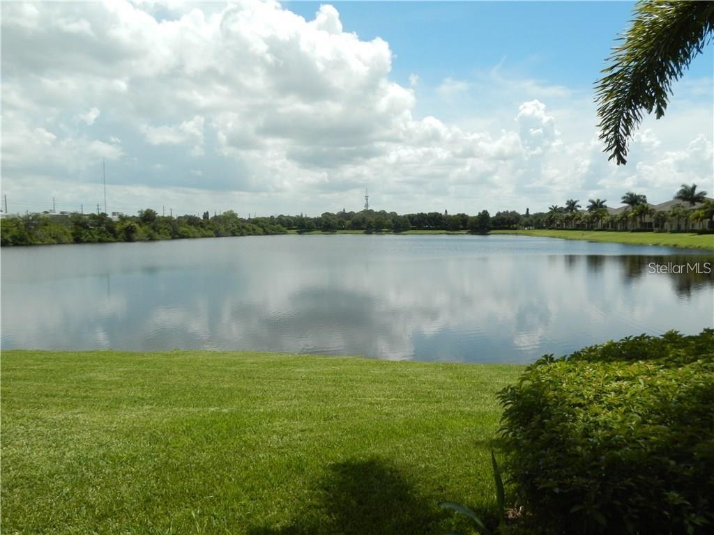 A grassy lawn overlooks a calm lake under a blue sky with scattered clouds — 3825 45TH TERRACE W UNIT 104, BRADENTON, FL