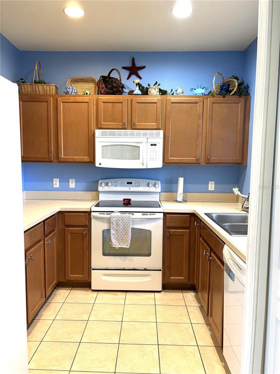 A kitchen features wood cabinets, a white stove, a microwave, and light-colored tile flooring — 3825 45TH TERRACE W UNIT 104, BRADENTON, FL