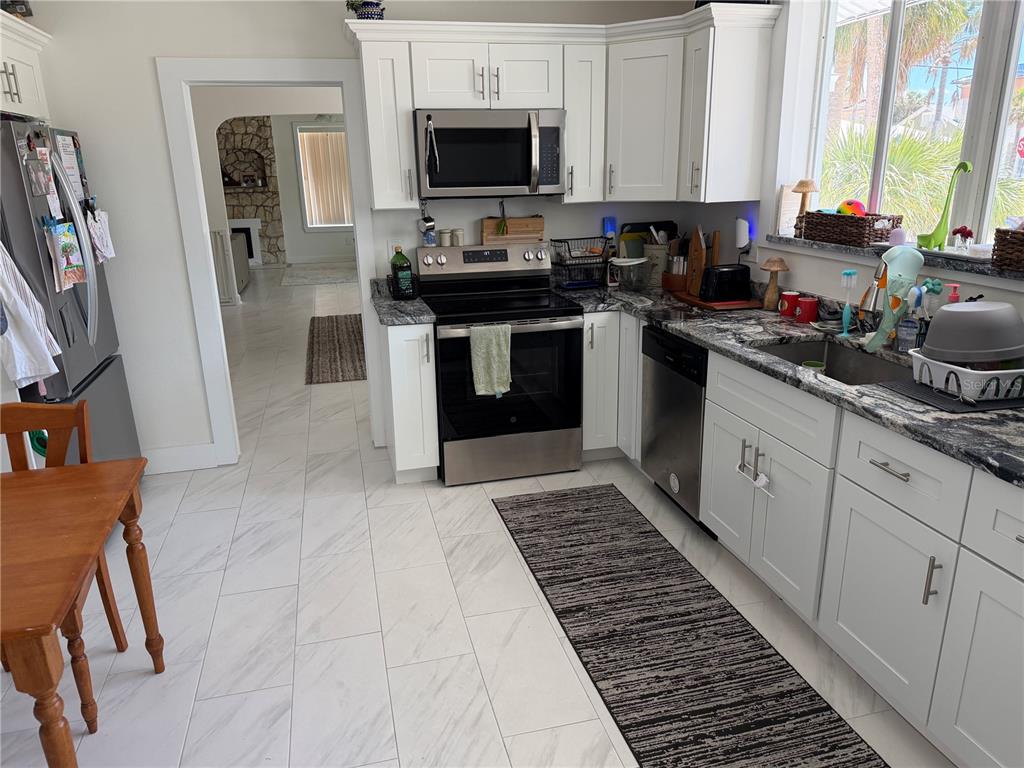 A kitchen features white cabinets, granite countertops, stainless steel appliances, and light-colored tile flooring — 850 MANDALAY AVENUE, CLEARWATER BEACH, FL